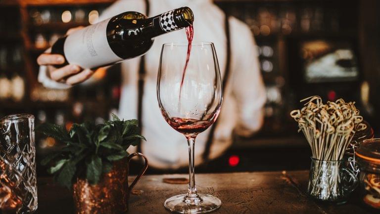 A bartender pours a red wine into a glass