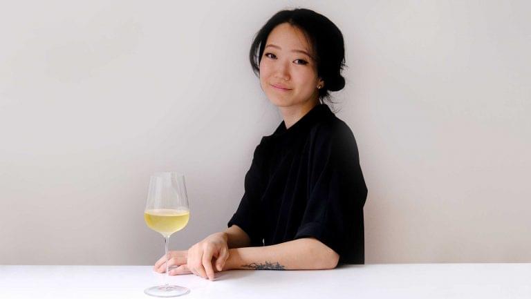 A headshot of Eun Hee Kwon against a white background. She sits with her arm resting on a surface with a glass of white wine next to her.