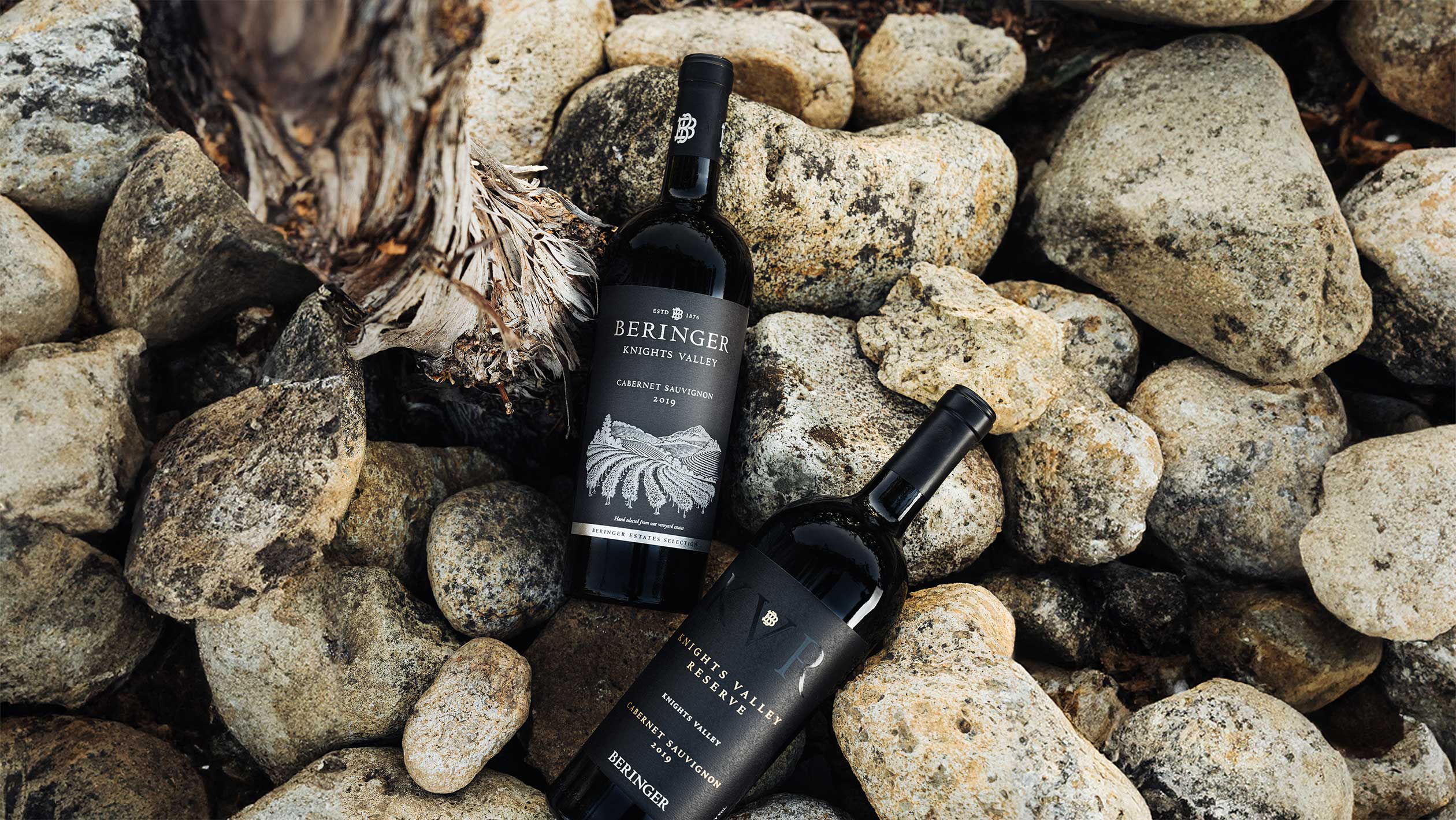 A closeup of two bottles of Beringer wine on top of a bed of rocks