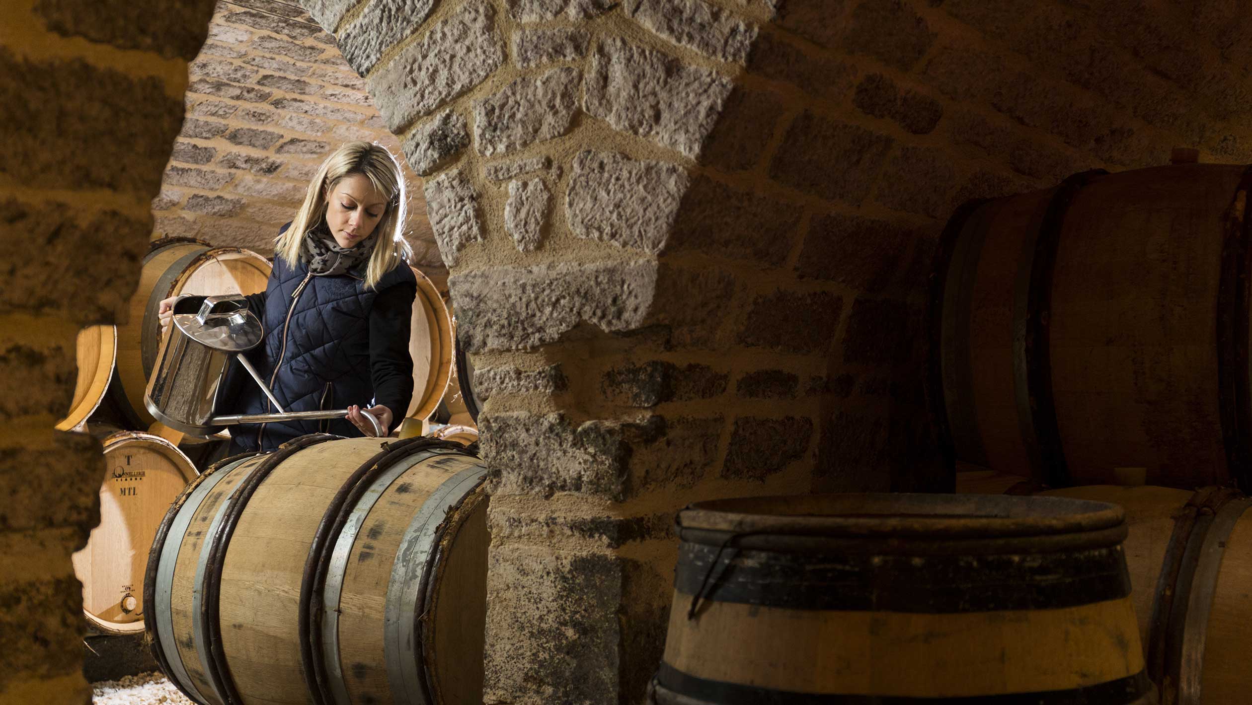 A winemaker measures ouillage for a barrel of wine